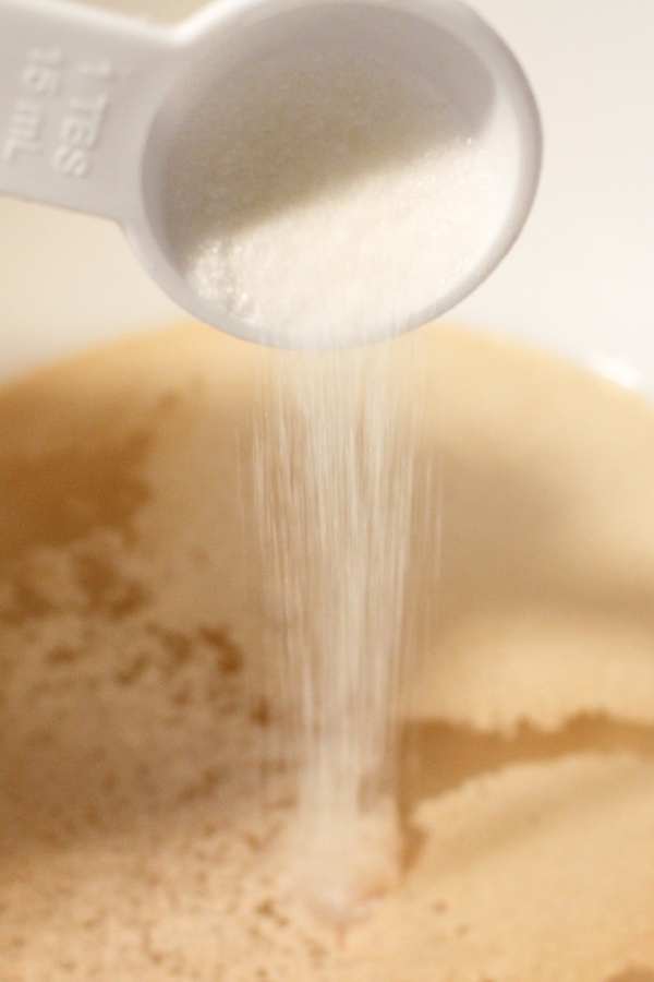 sugar pouring in a bowl of yeast for gluten free bagel recipe